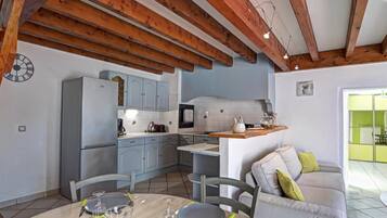 A kitchen with wooden beams, a dining table set for four, and a grey sofa in the living area.