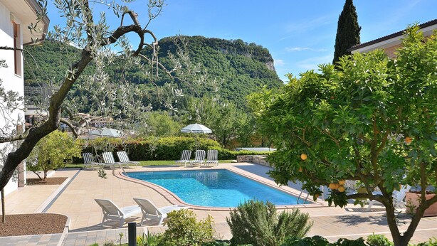 Une piscine entourée de chaises longues, de verdure et dominée par une chaîne de montagnes.