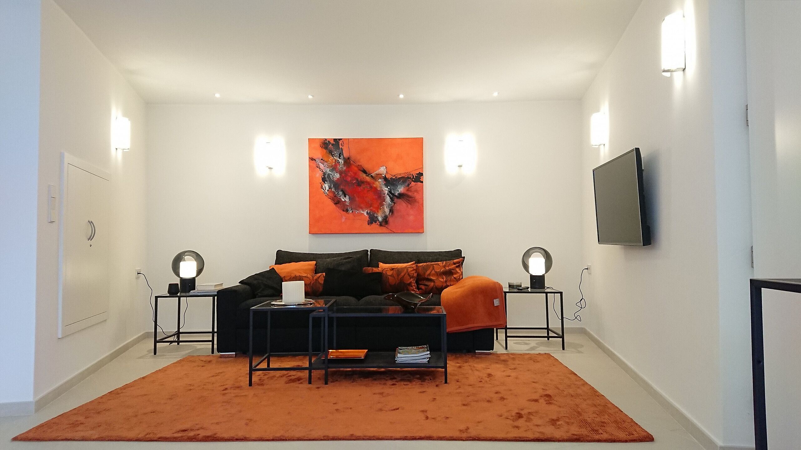 A modern bedroom with a black sofa, orange rug, and a large abstract painting.