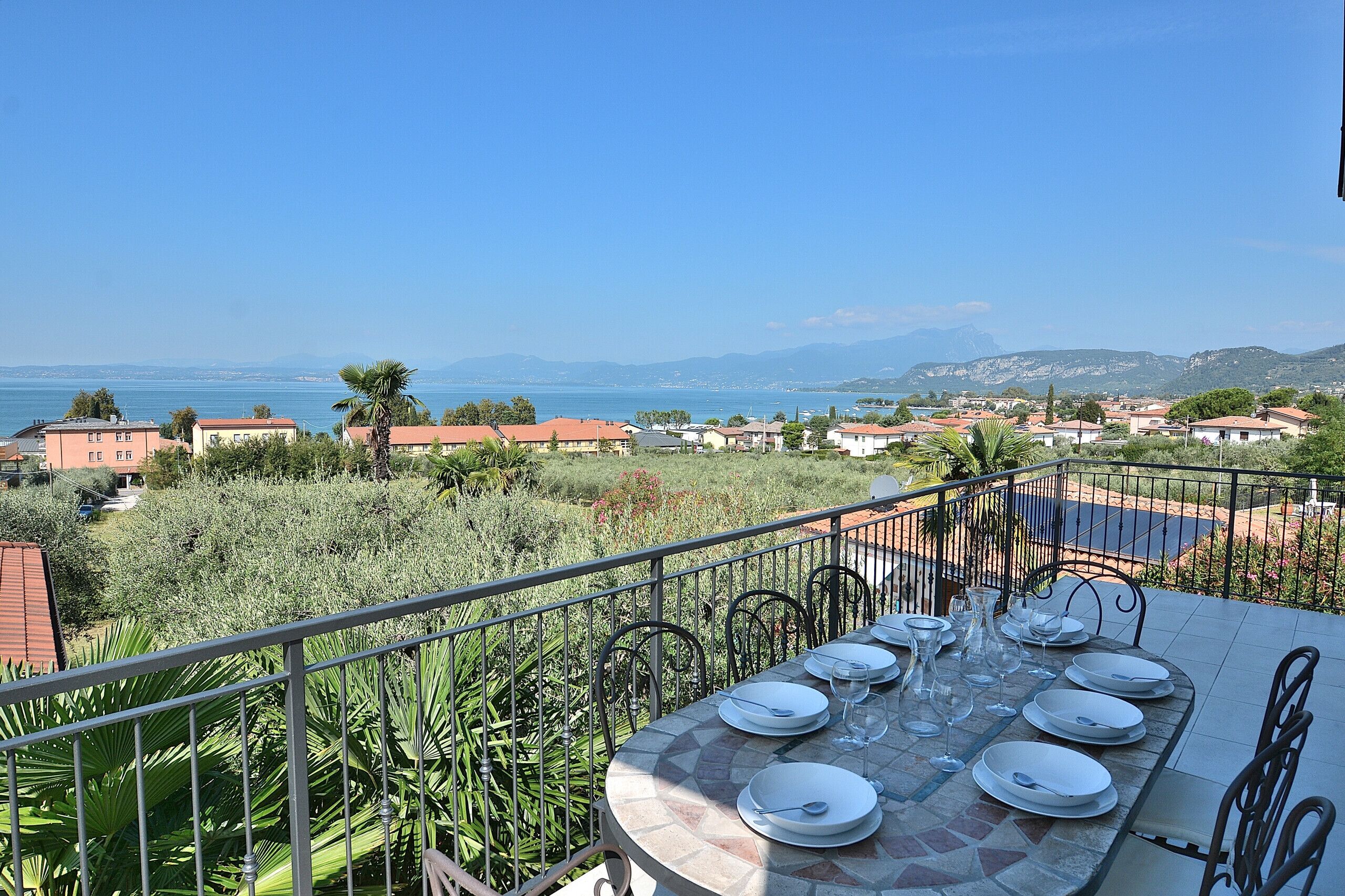 A terrace with a table set for dining, overlooking a coastal town and mountains.