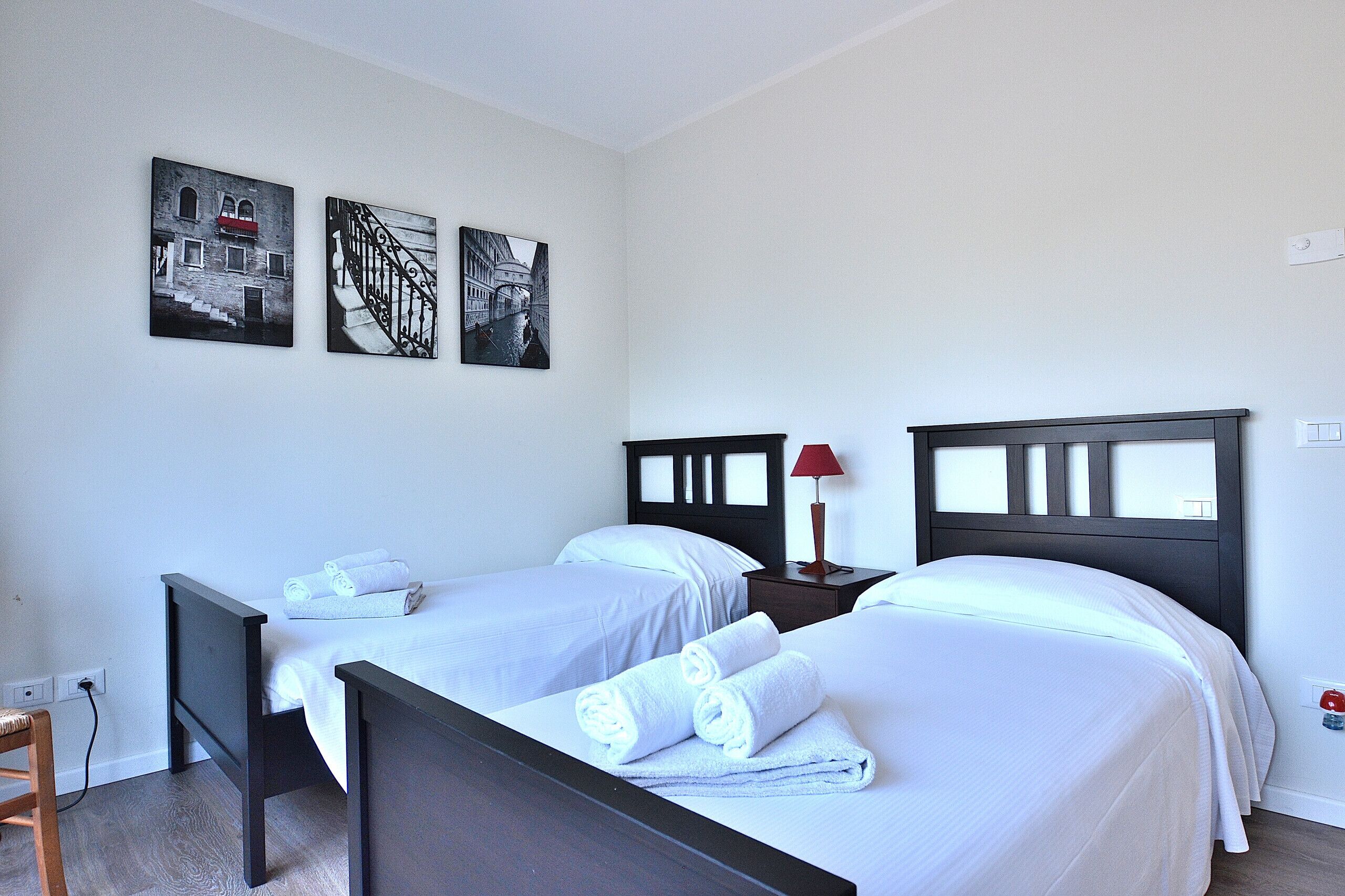 Habitació d'hotel amb dos llits, una tauleta de nit i obra d'art a la paret.