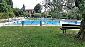 A swimming pool with a surrounding deck, benches, and a grassy area. - Villa Lisi With Pool (Bardolino)