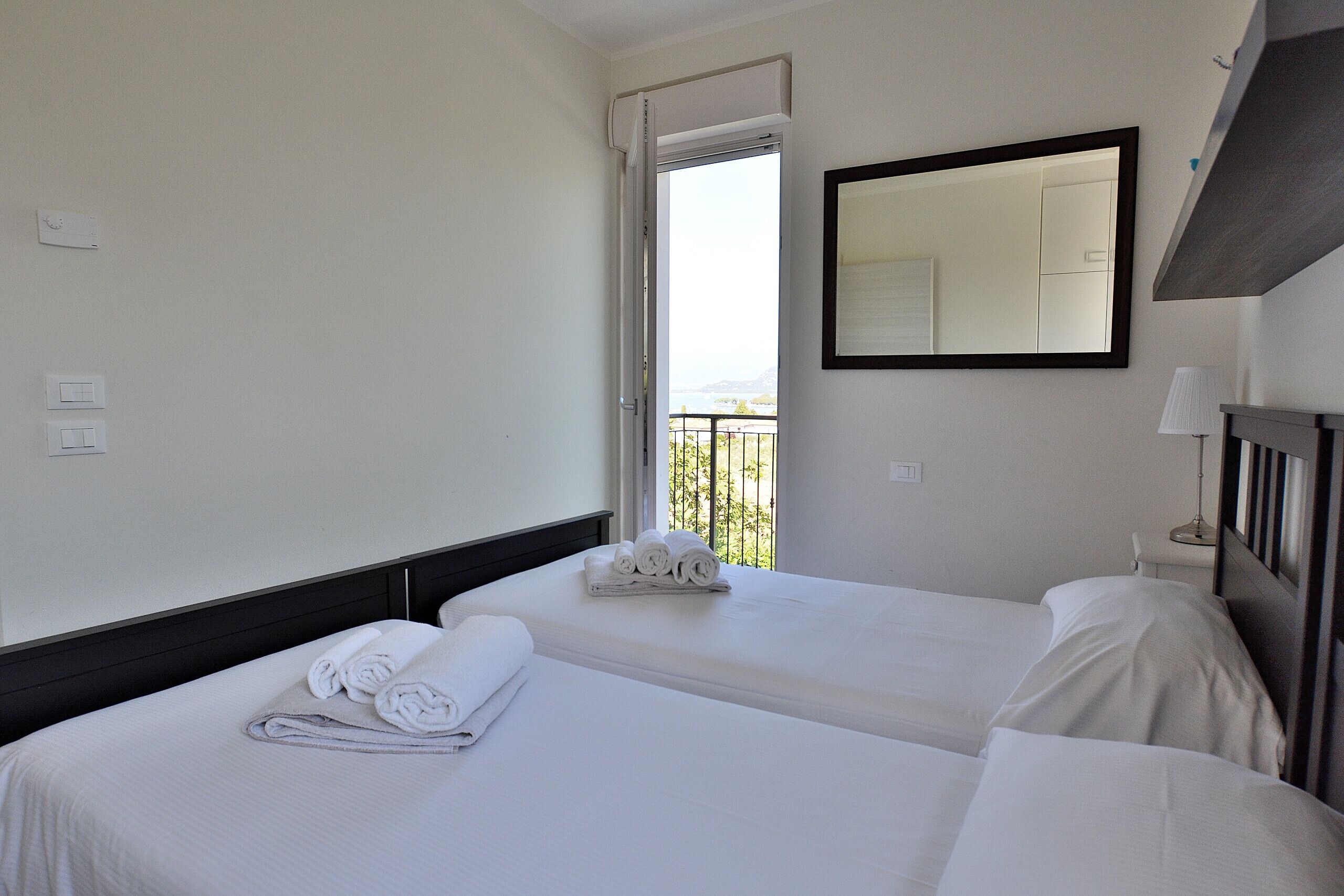 A hotel room with two beds, a large mirror, and a balcony with a view.
