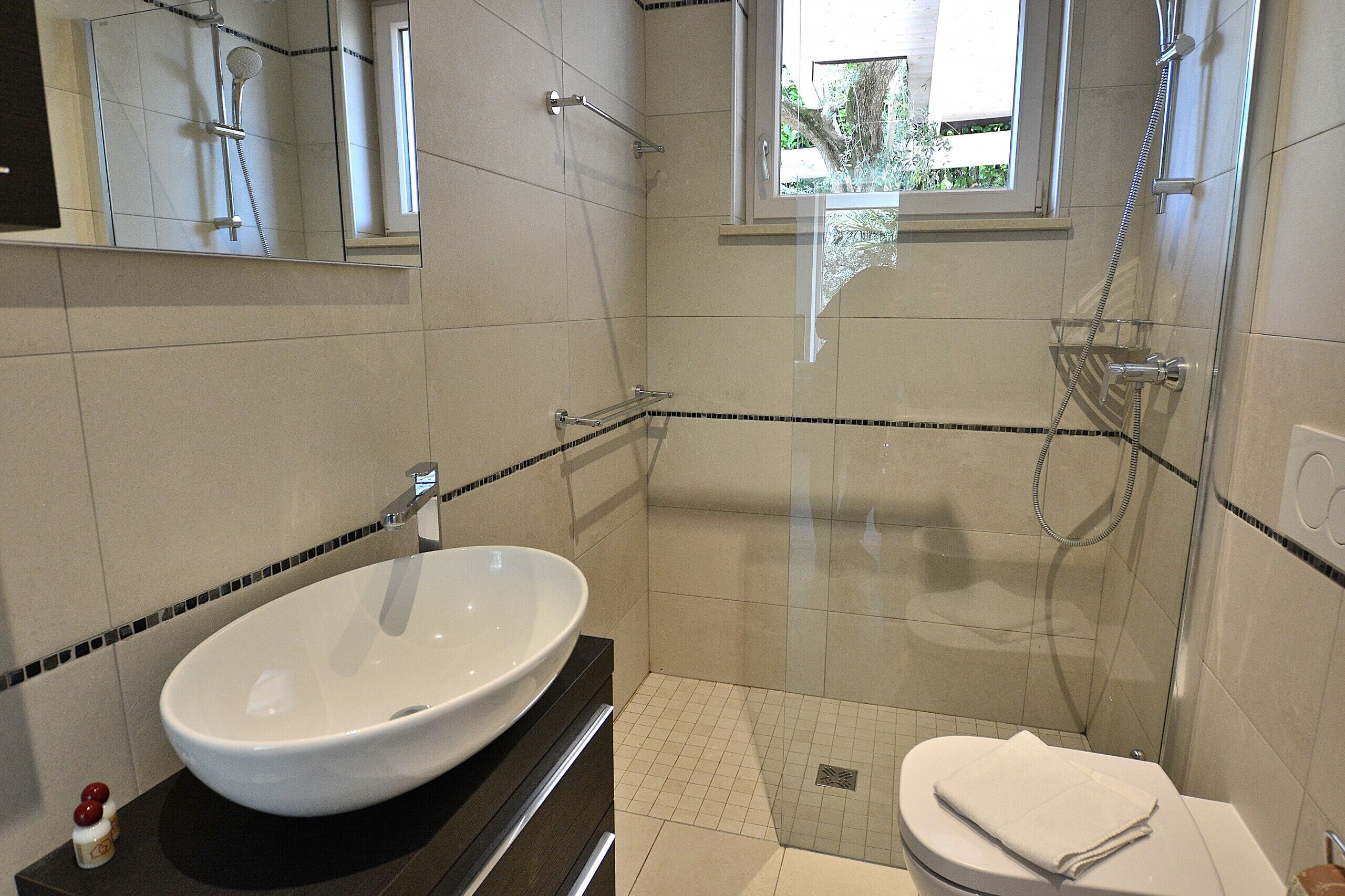 A modern bathroom with a large white sink, a glass-enclosed shower, and a toilet.