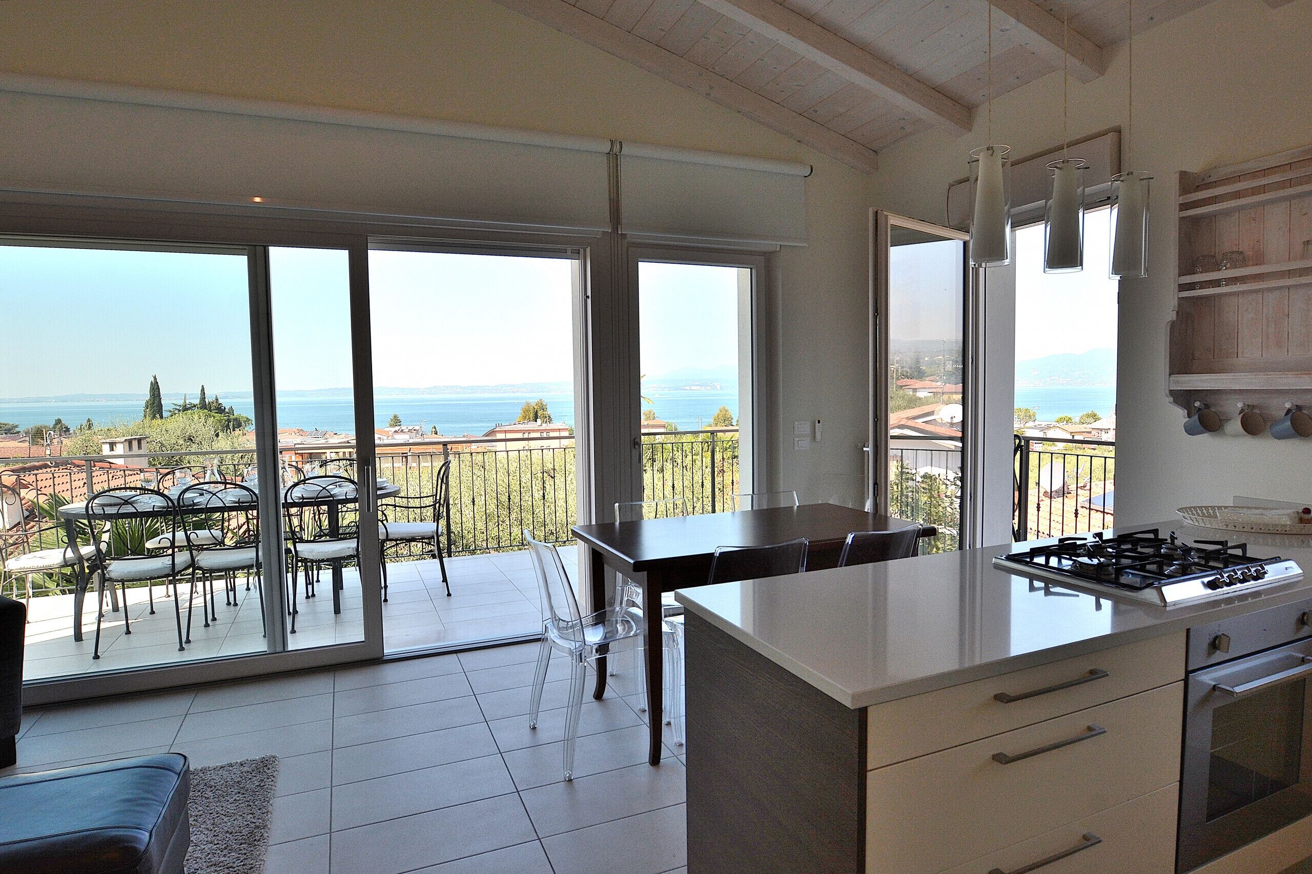 A modern kitchen with a large island, a dining area with chairs and a table, and a view of the sea through large windows.