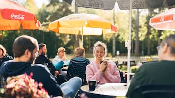 En grupp människor sitter vid bord under parasoller, och det finns utemöbler arrangerade för sittande.