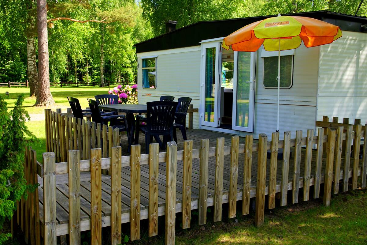 A mobile home with a deck, a table, and chairs.
