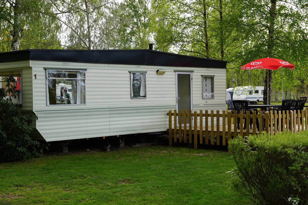 A mobile home with a fenced yard, a red umbrella, and a table with chairs.