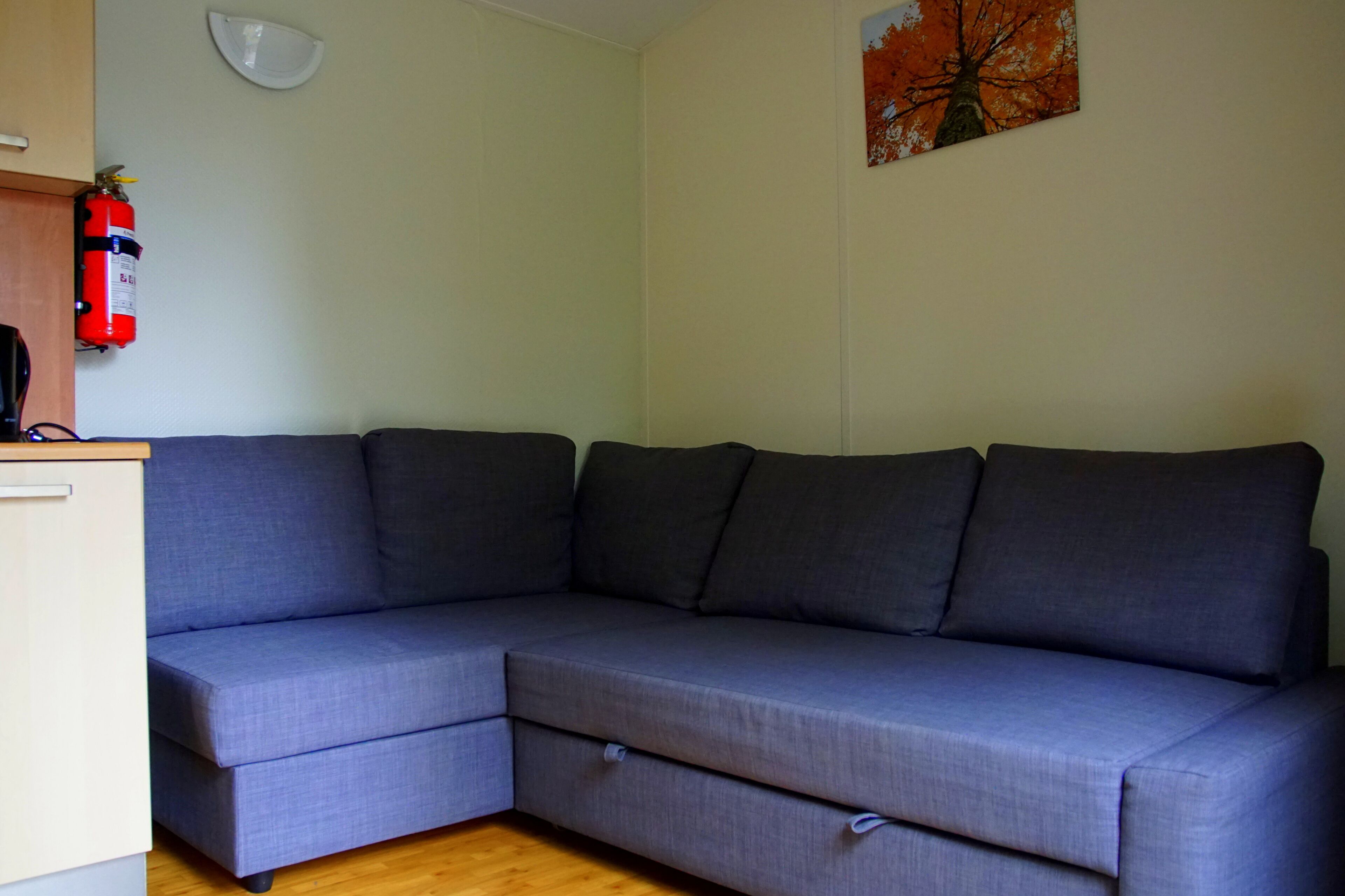 A grey sectional sofa with a small table and a fire extinguisher on the wall.