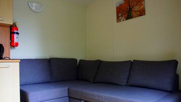 A grey sectional sofa with a small table and a fire extinguisher on the wall.