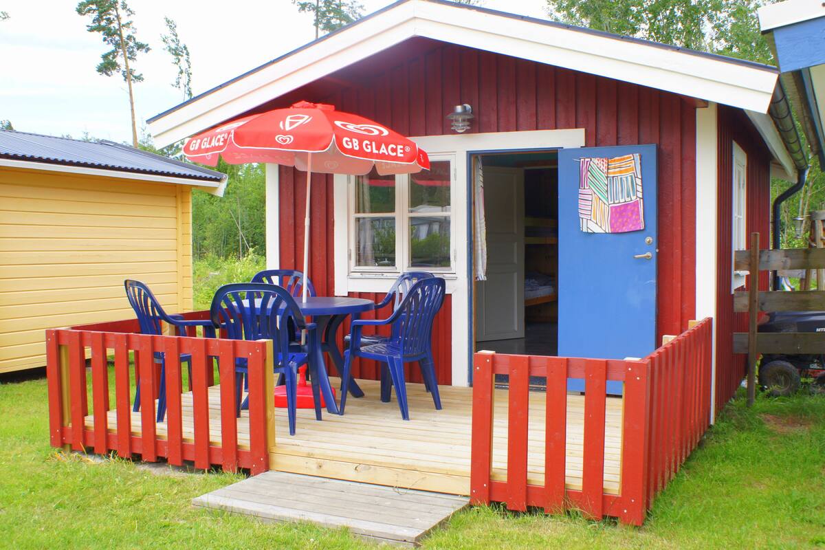 A small, red and white building with a wooden deck, blue chairs, and a red fence.