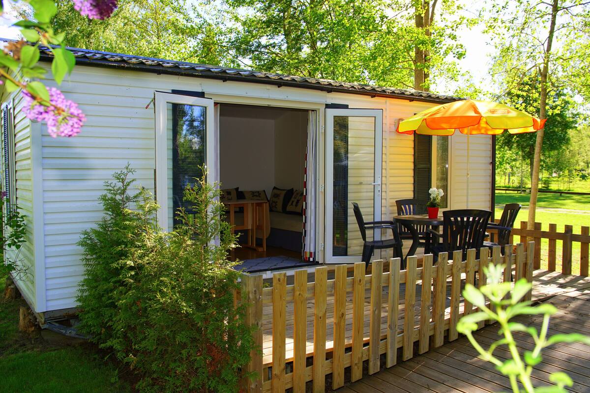 A small wooden cabin with an open door, a deck with chairs, and a table.
