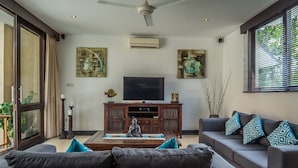 A living room with a sofa, a coffee table, a TV, and artwork on the walls. - Villa Kiaja (Kerobokan)