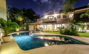 A modern house with a swimming pool, a covered patio, and lush greenery.