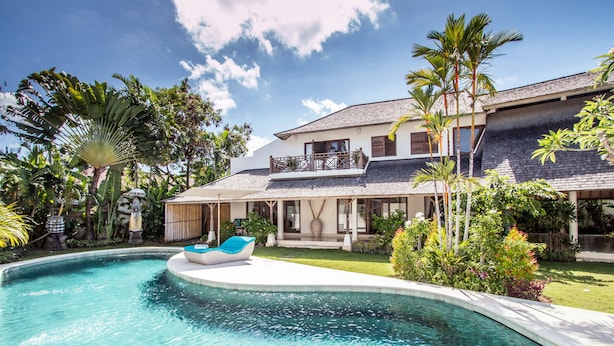 Uma casa grande com piscina, cercada por plantas tropicais e um céu claro.