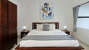A bedroom with a wooden bed, two bedside tables with lamps, a large abstract painting on the wall, and a window with curtains. - Villa Melati (Legian)
