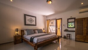 A spacious bedroom with a large bed, a bedside table with a lamp, a framed artwork on the wall, and a sliding door leading to a balcony. - Villa Cantik (Legian)