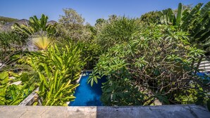 A swimming pool surrounded by lush greenery and a clear blue sky. - Villa Cantik (Legian)