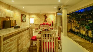 A dining area with a wooden table and chairs, a bar counter, and a mural of a tropical landscape. - Villa Airin (Canggu)