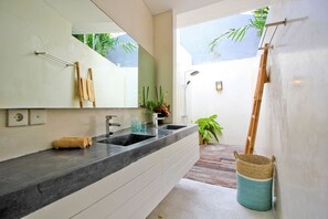 Un baño moderno con un espejo grande, dos lavamanos, una ducha y una pequeña planta.