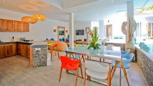 Une cuisine moderne avec des meubles en bois, un îlot central et un coin repas comprenant une table en verre et des chaises colorées.
