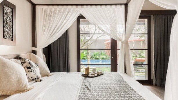 Ein Schlafzimmer mit einem großen Bett, Blick ins Freie und einem mit Vorhängen drapierten Fenster.