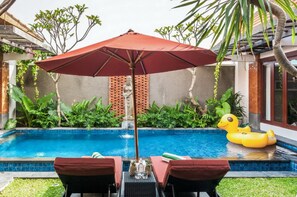 A swimming pool with a red umbrella, two lounge chairs, and a yellow inflatable duck.