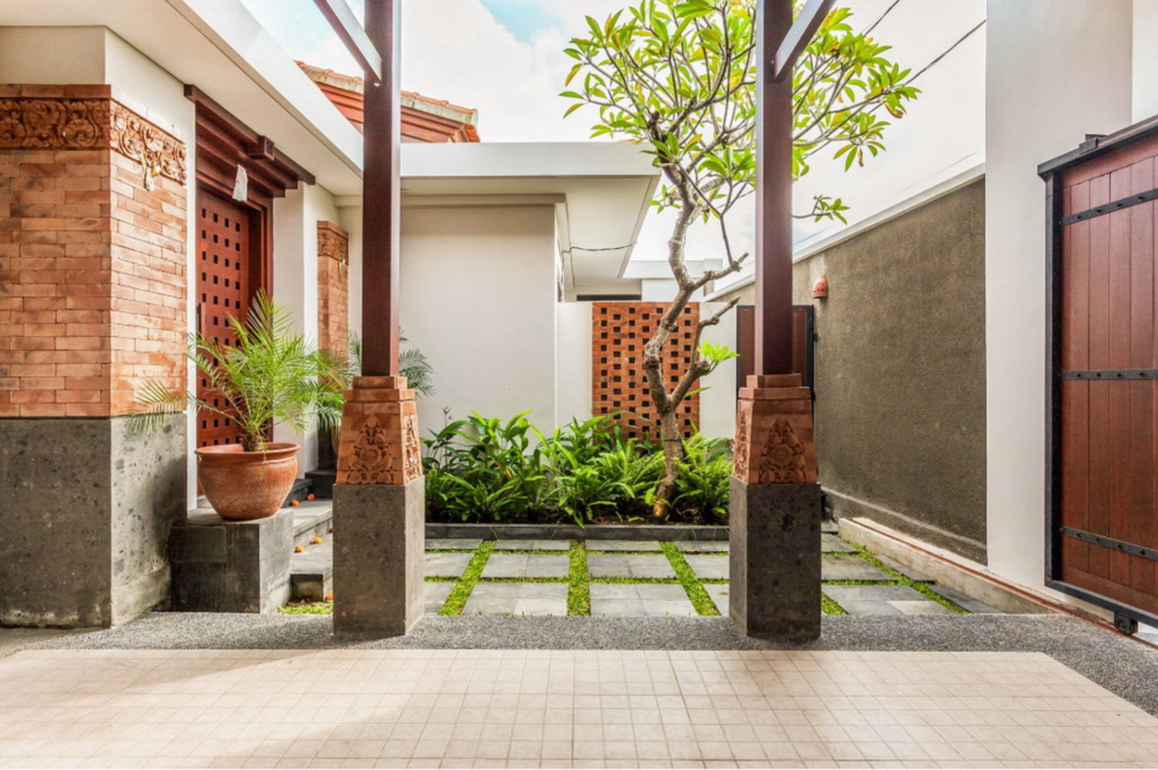 A courtyard with a brick wall, a wooden door, and a potted plant.