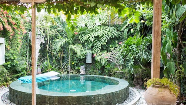 A circular hot tub surrounded by a stone border, with a wooden pergola overhead and lush tropical plants in the background. - Villa Wonderland (Seminyak)