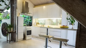 A modern kitchen with white cabinets, a built-in oven, and a bar area with stools. - Villa Wonderland (Seminyak)