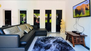 Un salon moderne avec un canapé en cuir noir, un tapis noir et blanc, une table d’appoint en bois sur laquelle se trouve un téléviseur, et une statue.
