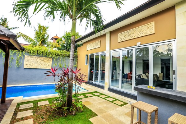 Un espacio exterior moderno con piscina, un porche cubierto y una zona de estar con mobiliario de mimbre.