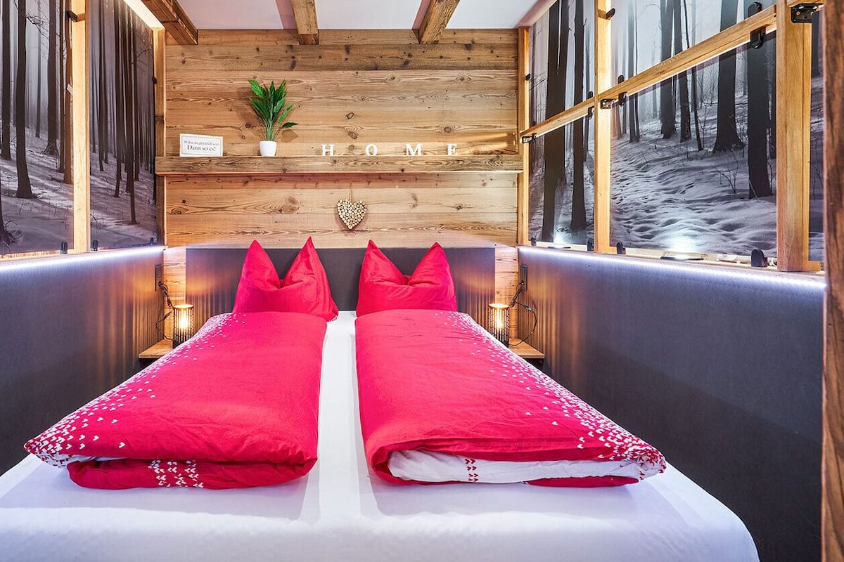 A room with a bed, a wooden wall, and a window with a view of trees.