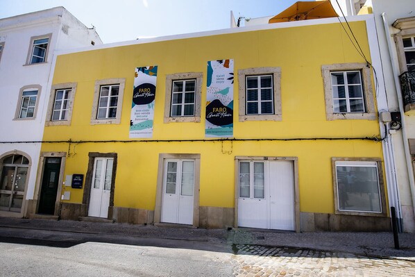 A yellow building with multiple windows and doors, banners advertising a guest house, and a cobblestone street. - Faro Guest House (Faro)