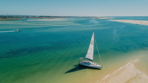 Un voilier sur une mer calme, avec une plage de sable au premier plan.