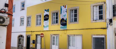 A yellow building with multiple windows and doors, featuring banners advertising a guest house.