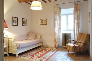 A bedroom with a bed, a chair, a radiator, and a window with curtains.