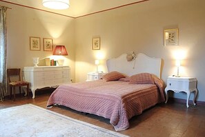 A bedroom with a large bed, two bedside tables with lamps, a dresser, and a chair.