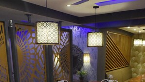 A restaurant with a modern interior, featuring white chairs, wooden tables, and decorative lighting fixtures.