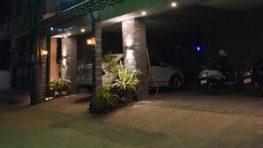 A hotel entrance with a neon sign, a covered parking area, and potted plants.