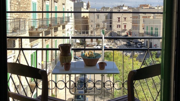 A balcony with two wooden chairs and a small table, overlooking a cityscape with stone buildings and a clear sky. - Chantale's posada (Giovinazzo)