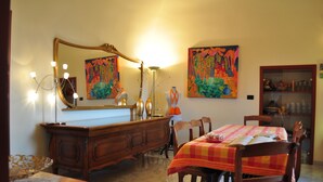A room with a wooden dresser, a large mirror, a dining table with chairs, and two colorful paintings on the wall. - Chantale's posada (Giovinazzo)