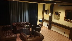 A cozy room with a dark curtain, a brown leather sofa, a small round table with a vase, and a wall-mounted TV. - Hotel Gaya (Bad Soden am Taunus)