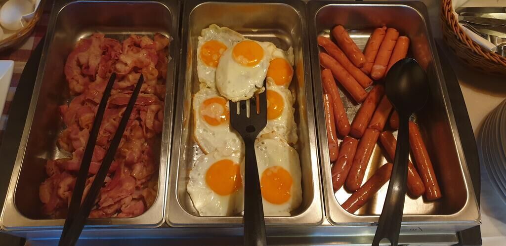 Ein Buffet mit drei Tabletts: Speck, Eier und Würstchen.
