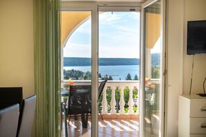 Un balcon avec vue sur un lac, une table avec des chaises et un téléviseur fixé au mur.