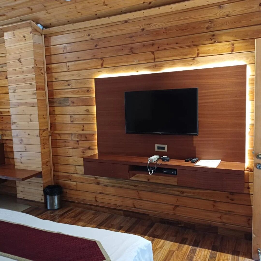 Habitación con paneles de madera, televisor de pantalla plana montado en la pared, una mesita con toma de corriente y un cubo de basura.