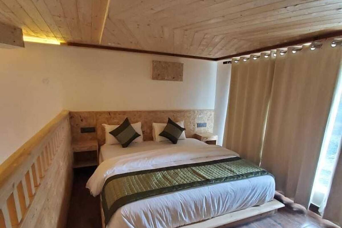 Ein Zimmer mit Holzwänden, einem Bett, Holzboden und einem Fenster mit Vorhängen.
