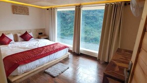 A wooden cabin bedroom with a bed, a small table, and a window with curtains. - Seven Hills Hotels and Resorts (Lansdowne)