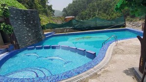 A swimming pool with a tiled edge, surrounded by a stone wall and greenery. - Seven Hills Hotels and Resorts (Lansdowne)