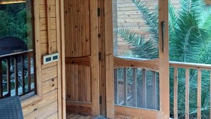 A wooden cabin with a large glass door, a wooden deck, and a view of greenery outside. - Seven Hills Hotels and Resorts (Lansdowne)